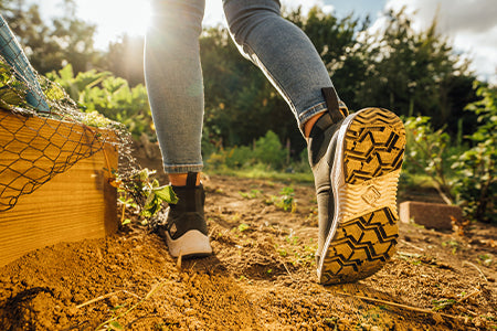 Eine Person, die Muck Boots trägt, geht durch einen Schrebergarten 
