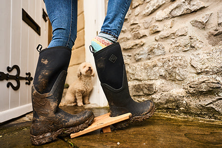 Person, die einen Gummistiefel mit einem Stiefelknecht auszieht