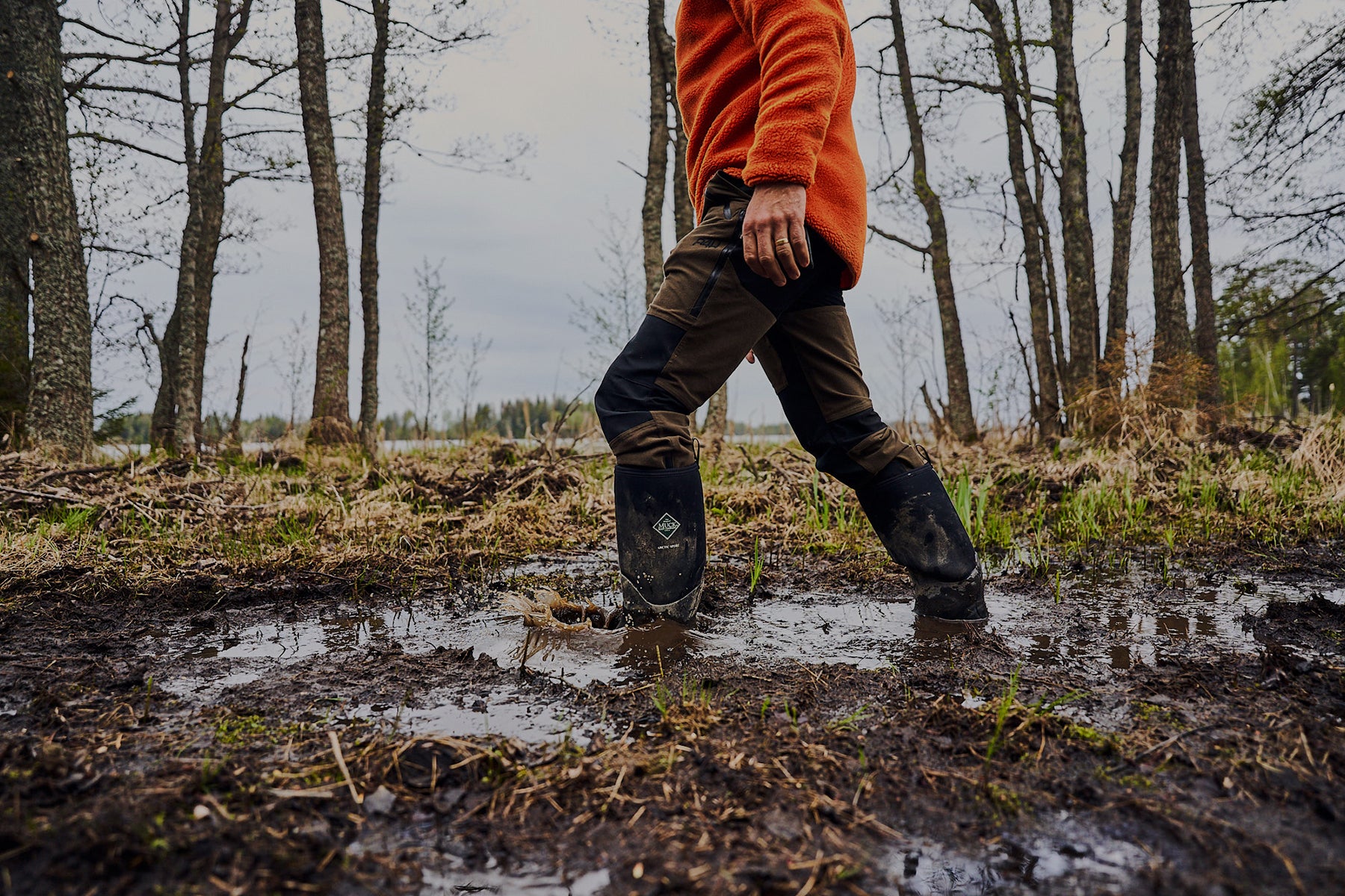 Mann, der in einem Paar Muck Boots durch schlammigen Boden läuft