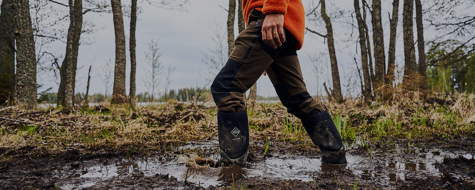 Mann, der in einem Paar Muck Boots durch schlammigen Boden läuft
