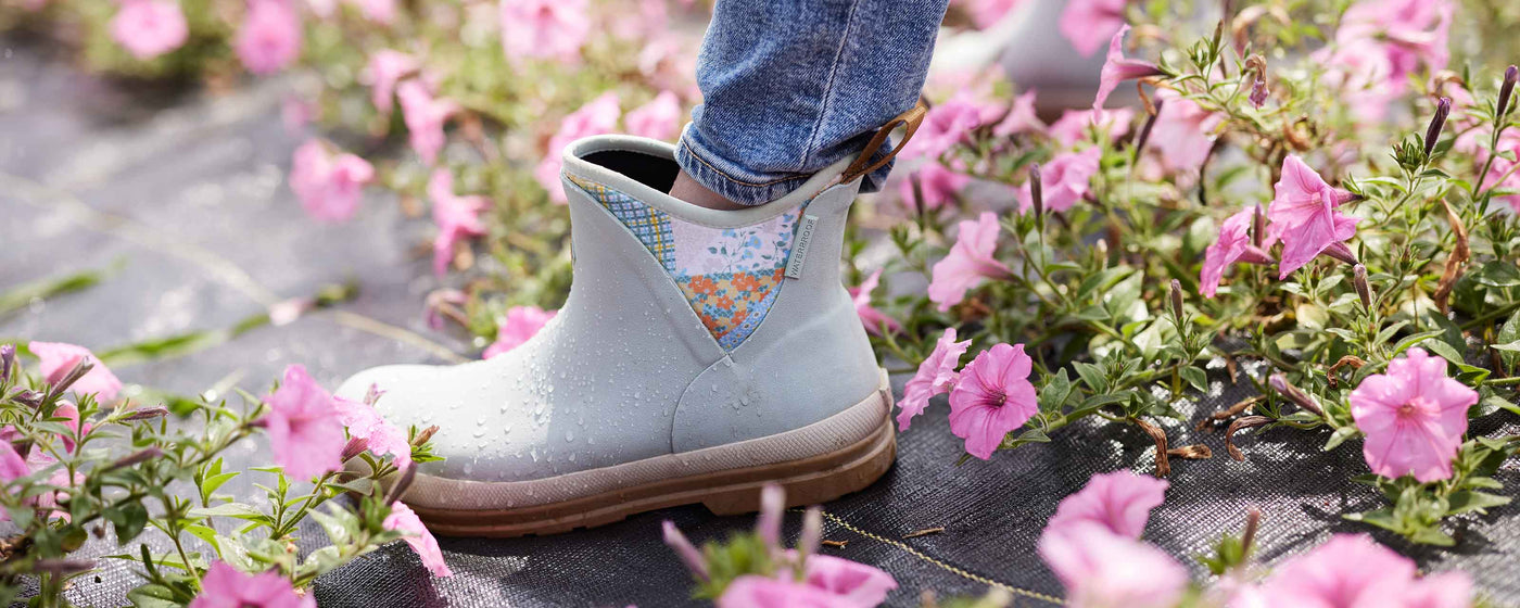 Close up image of a person wearing a pair of Muck Boots Muck Originals Boot surrounded with pink flowers