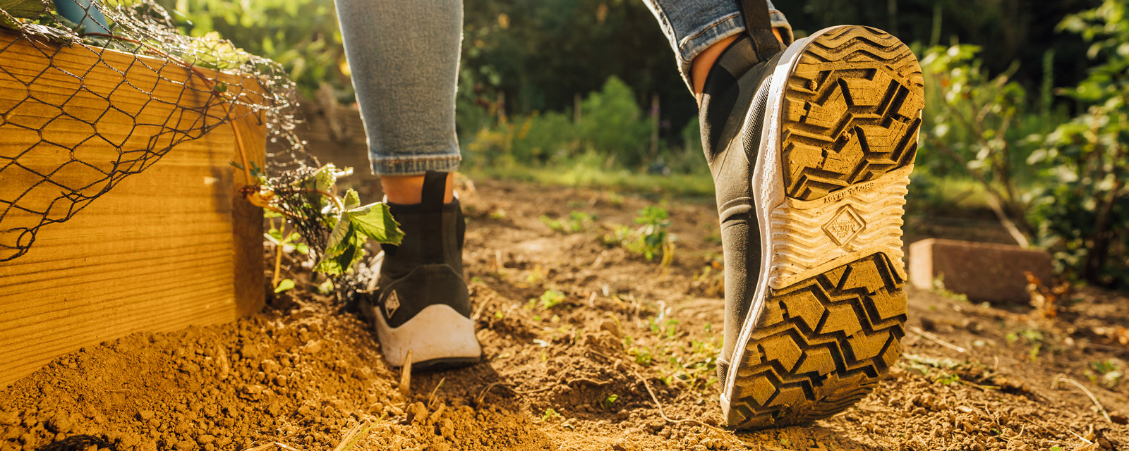 Eine Person, die Muck Boots trägt, geht durch einen Schrebergarten 