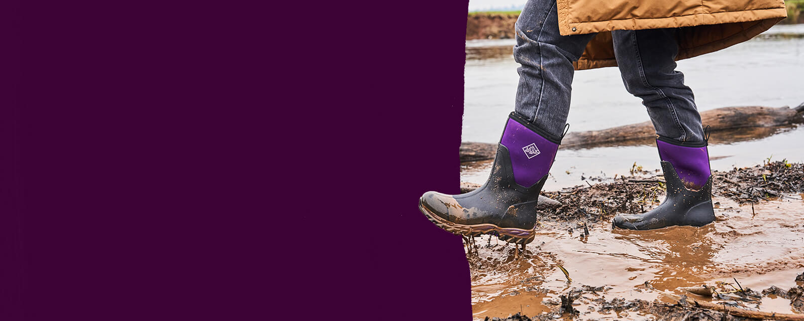 Person wearing a pair of Muck Boots Women's Arctic Sport II boots in black acai, walking through a muddy puddle.