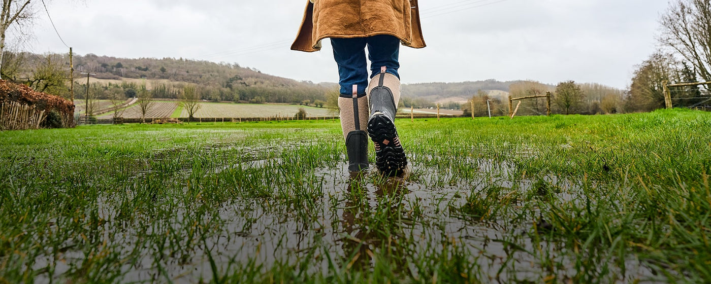 Woman walking through a wet field, wearing a pair of Muck Boots Arctic Sport II Wellingtons