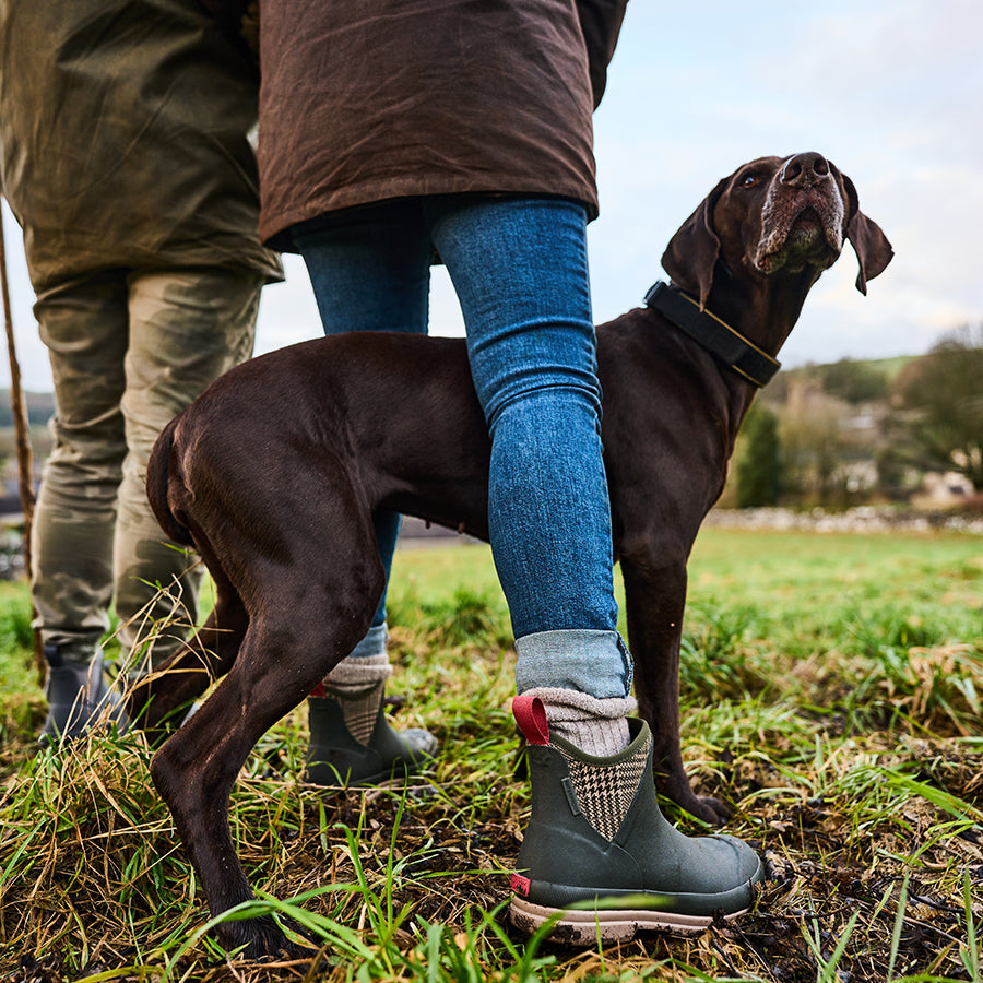 Two people stood in a field, wearing Muck Boot ankle boots with a large brown dog between them