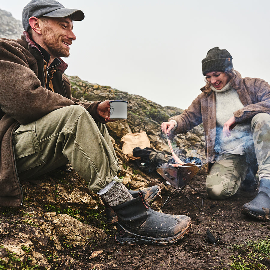 Man and woman cooking outside with a portable stove, wearing Muck Boots