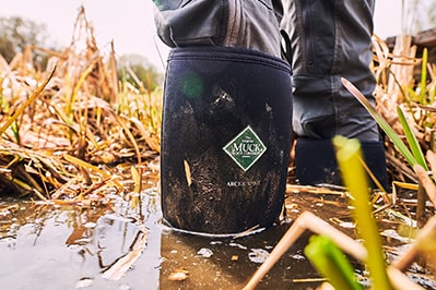 Nahaufnahme einer Person, die in hohem Wasser steht und ein Paar Muck Boots Arctic Sport Gummistiefel trägt