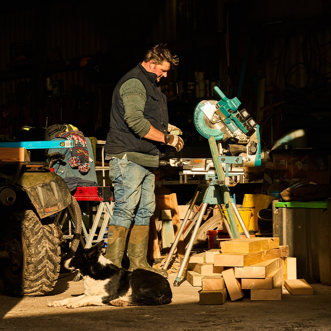 Man wearing a pair of Muck Boots wellingtons, in a workshop with a dog