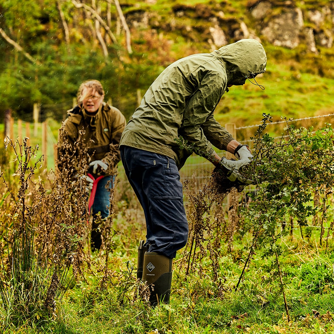 Man and woman gardening in the rain. The man is wearing a pair of Muck Boots Muckmaster wellington boots