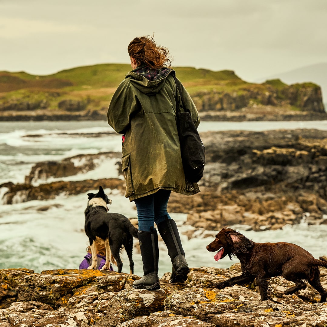 Woman wearing Muck Boots wellingtons, walking two dogs along a rocky beach